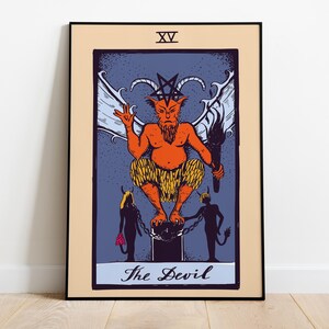 Puede incluir: Impresión enmarcada de una carta del tarot que presenta una figura del diablo con cuernos, alas y una antorcha, en tonos naranja, azul y amarillo. La carta está etiquetada como "The Devil" y tiene el número romano XV en la parte superior. La obra de arte está sobre un fondo beige.