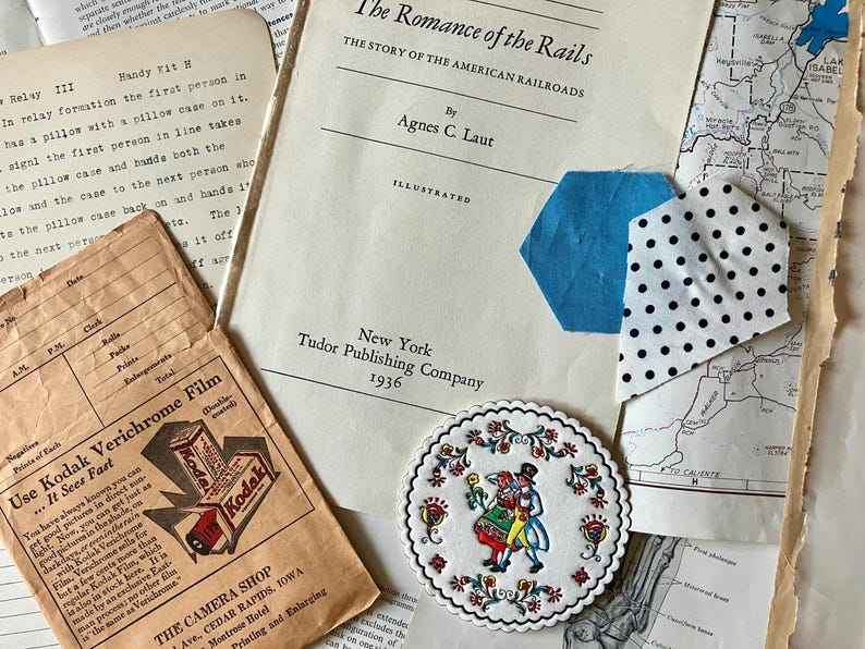 K&ouml;nnte beinhalten: Ein Vintage-Buch mit dem Titel "The Romance of the Rails: The Story of the American Railroads" von Agnes C. Laut, illustriert und ver&ouml;ffentlicht 1936 von Tudor Publishing Company in New York. Der Buchumschlag ist wei&szlig; mit schwarzem Text. Ein blauer und wei&szlig;er Stoffrest mit wei&szlig;en Punkten befindet sich auf dem Umschlag.