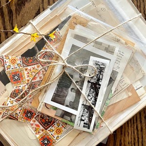 K&ouml;nnte beinhalten: Ein B&uuml;ndel Vintage-Ephemera, darunter alte Fotos, Briefe und gemustertes Papier, zusammengebunden mit Schnur. Das B&uuml;ndel ist in eine durchsichtige Plastikt&uuml;te verpackt und hat eine rustikale, Vintage-&Auml;sthetik.