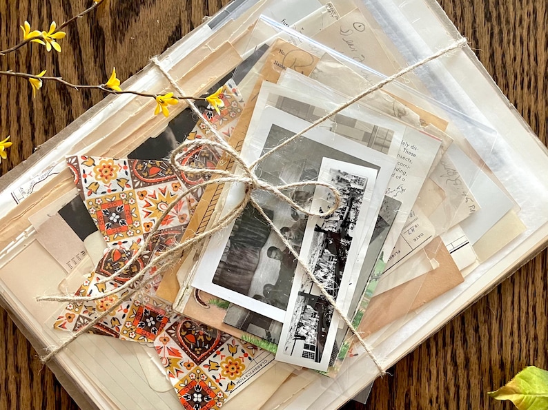K&ouml;nnte beinhalten: Ein B&uuml;ndel Vintage-Ephemera, darunter alte Fotos, Briefe und gemustertes Papier, zusammengebunden mit Schnur. Das B&uuml;ndel ist in eine durchsichtige Plastikt&uuml;te verpackt und hat eine rustikale, Vintage-&Auml;sthetik.