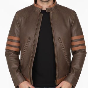 May include: Brown leather jacket with tan stripes on the sleeves and a tan collar. The jacket has a zipper closure and two front pockets. The person is wearing a black shirt and blue jeans.