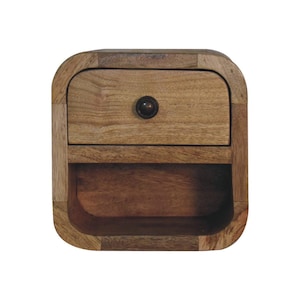 Könnte beinhalten: Ein kleiner Nachttisch aus Holz mit einer Schublade und einem offenen Regal darunter. Der Nachttisch hat eine abgerundete, quadratische Form und ist aus hellbraunem Holz mit einem dunkelbraunen Knopf an der Schublade gefertigt. Die Holzmaserung ist sichtbar.