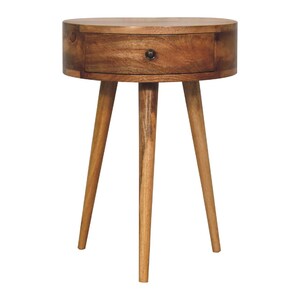 Könnte beinhalten: Ein runder Nachttisch aus hellem Holz mit einer Schublade und drei angewinkelten Beinen. Der Tisch ist aus hellbraunem Holz gefertigt und hat einen dunklen Knopf an der Schublade. Die Beine sind schlank und verjüngt, für einen Mid-Century-Modern-Look. Durchmesser ca. 50 cm.