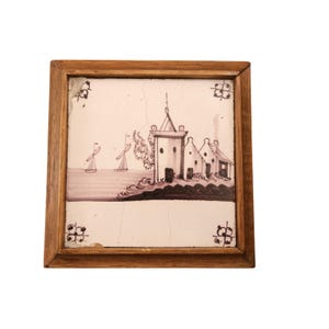 May include: A framed, square tile featuring a coastal scene in shades of white and purple. The artwork depicts a tower, houses, sailboats, and a windmill. The tile is set within a wooden frame, showcasing a vintage aesthetic.