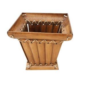 May include: A square, light brown bamboo basket with a flared shape. The basket is constructed from vertical bamboo slats, with woven accents around the rim and base. The basket has a natural, rustic appearance.