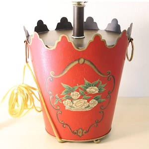 May include: A red decorative lamp with a floral design. The lamp has a bucket-like shape with a scalloped top and gold accents. A yellow cord and plug are attached.