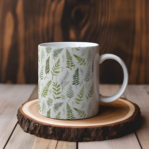 May include: White ceramic mug with a repeating pattern of green fern leaves. The mug has a curved handle and is on a round wooden coaster with a natural bark edge. The background is a wooden surface.