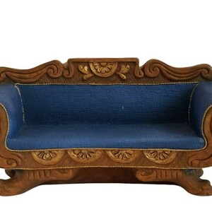 May include: Miniature blue sofa with ornate brown wooden frame. The sofa features a blue fabric seat and back, with gold trim and decorative carvings. A small, detailed piece of furniture.