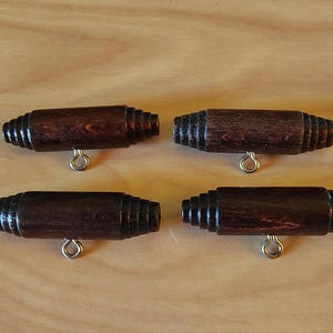 May include: Four dark brown wooden cabinet knobs with a cylindrical shape and silver-colored metal bails. The knobs have a series of ridges at each end and are arranged on a light brown wooden surface.