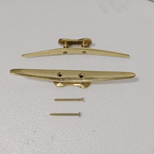 以下が含まれることがあります： 2本のネジが付いた金色の金属製のボートクリート。クリートはボートのデッキに取り付けるように設計されています。