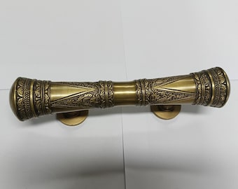 May include: A decorative brass door handle with an ornate design. The handle is cylindrical and has a textured surface.