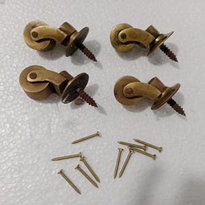 May include: A set of four antique brass casters with screws. Each caster features a curved design and a small wheel. The screws are brass-coloured and have a pointed end. Suitable for furniture restoration or vintage projects.
