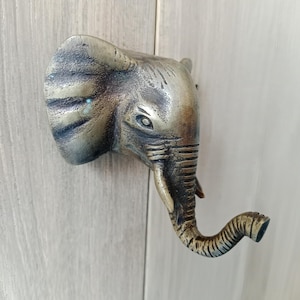 Puede incluir: Un pomo de puerta de bronce con forma de cabeza de elefante con una trompa texturizada y una oreja detallada.