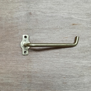 May include: A silver metal toilet paper holder with a curved arm and a rectangular base. The holder is mounted on a wooden wall.