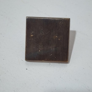 May include: A square-shaped, brushed brass cabinet knob with a slightly rounded edge.