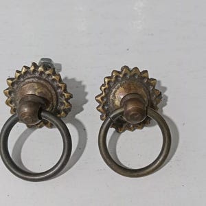 May include: Two antique brass drawer pulls with a ring handle and a decorative starburst design.
