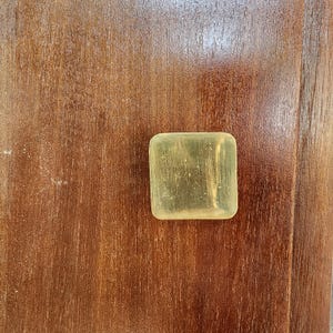 Könnte beinhalten: Ein quadratischer, messingfarbener Türknauf an einer Holztür.