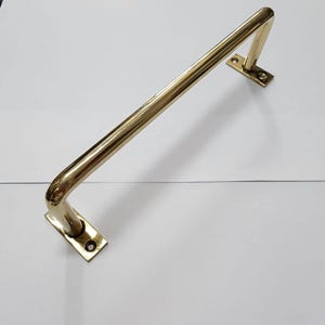 以下が含まれることがあります： 丸みを帯びたエッジとシンプルなデザインの磨かれた真鍮製のタオルバー。バーは2つの長方形のプレートで壁に取り付けられています。