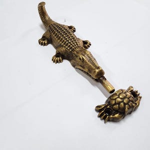 Peut inclure: Un butoir de porte en métal doré en forme de crocodile avec un corps texturé détaillé. La bouche du crocodile est ouverte et une tortue en métal doré séparée est attachée à la bouche du crocodile.