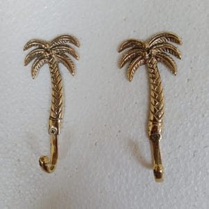 May include: Two gold palm tree shaped hooks. The hooks are designed to look like palm trees with a hook at the bottom of the trunk.