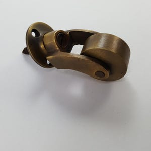 May include: A brass-toned metal furniture caster featuring a circular mounting plate with two screw holes, a swivel joint mechanism, and a single cylindrical wheel. The hardware has a brushed, aged finish with visible dark metal screw threads.