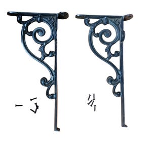 Könnte beinhalten: Zwei schwarze Metall-Regalhalterungen mit verzierten Schnörkeldesigns. Jede Halterung enthält Montageschrauben.