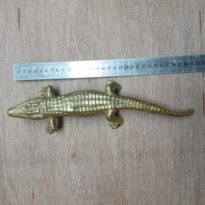 May include: A gold-colored alligator figurine with a textured surface. The figurine is approximately 28 inches long.