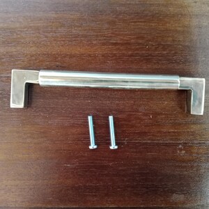 May include: A silver cabinet pull with a rectangular shape and rounded edges. The pull comes with two silver screws.