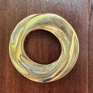 May include: A gold-colored metal ring with a swirling, textured design. The ring is round and has a hole in the center.