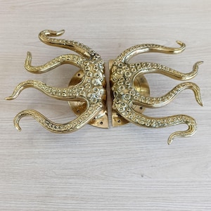 May include: A pair of brass door handles shaped like octopuses. The handles are detailed with textured surfaces and have a polished gold finish.