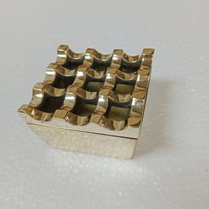 Peut inclure: Un cendrier en métal doré avec un motif en grille et un bord ondulé. Le cendrier est de forme carrée et a une surface texturée.