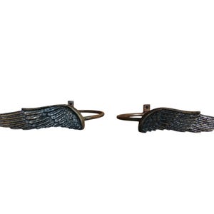 May include: A pair of decorative curtain rod finials in the shape of angel wings. The wings are made of metal and have a silver finish.