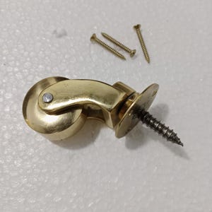 May include: A gold-toned caster wheel with a screw for attaching to furniture. The wheel is made of metal and has a smooth, polished finish. The screw is also made of metal and has a silver finish.