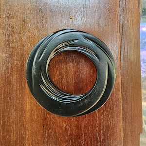 May include: A black circular door knocker with a swirling design. The knocker is mounted on a wooden door.