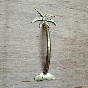 May include: A gold palm tree shaped door handle with a curved trunk and a cloud-shaped base.