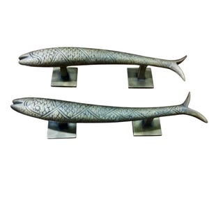 Op de afbeelding: Een paar antieke messing deurgrepen in de vorm van een vis met ingewikkelde details. De grepen zijn gemonteerd op vierkante bases.