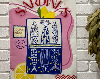 Può includere: Un canovaccio da cucina in cotone bianco con un design a sardine rosa e blu. Il canovaccio presenta la parola "SARDINE" in rosso, una scatola di sardine con illustrazioni di pesci e un limone. È visibile anche il testo "cotton reborn".