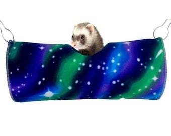 May include: A blue and green fleece ferret hammock with a white star pattern. A ferret is peeking out of the hammock.