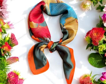May include: A colorful silk scarf with a geometric pattern in shades of red, orange, green, blue, and gold. The scarf is tied in a knot and the ends are hanging down.