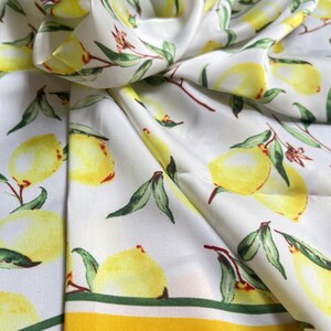 May include: White silk scarf with a yellow lemon print and a yellow border. The lemons are arranged in a repeating pattern on the scarf.