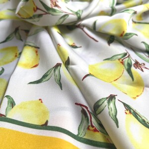 May include: White fabric with a yellow and green lemon print. The fabric has a yellow border.