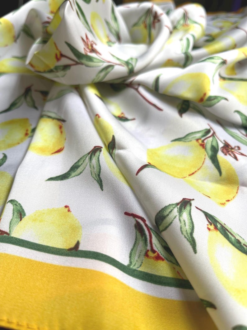May include: White fabric with a yellow and green lemon print. The fabric has a yellow border.
