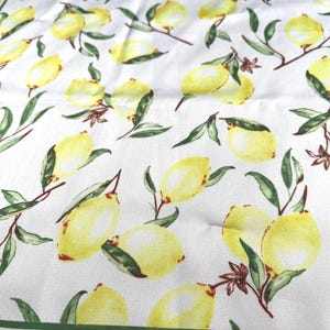 May include: White fabric with a yellow border and a repeating pattern of yellow lemons with green leaves.