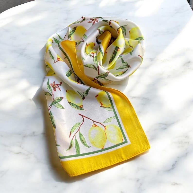May include: A white silk scarf with a yellow border and a lemon print. The lemons are yellow with green leaves.