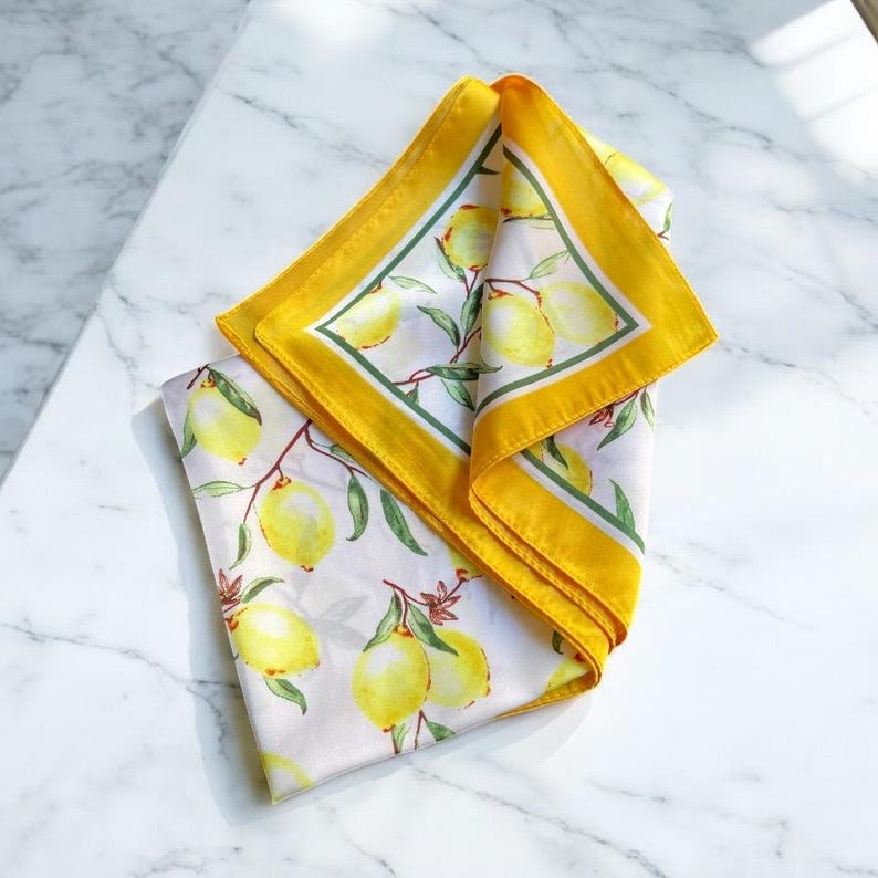 May include: A yellow silk scarf with a white background and a lemon print. The scarf has a yellow border with a green inner border.