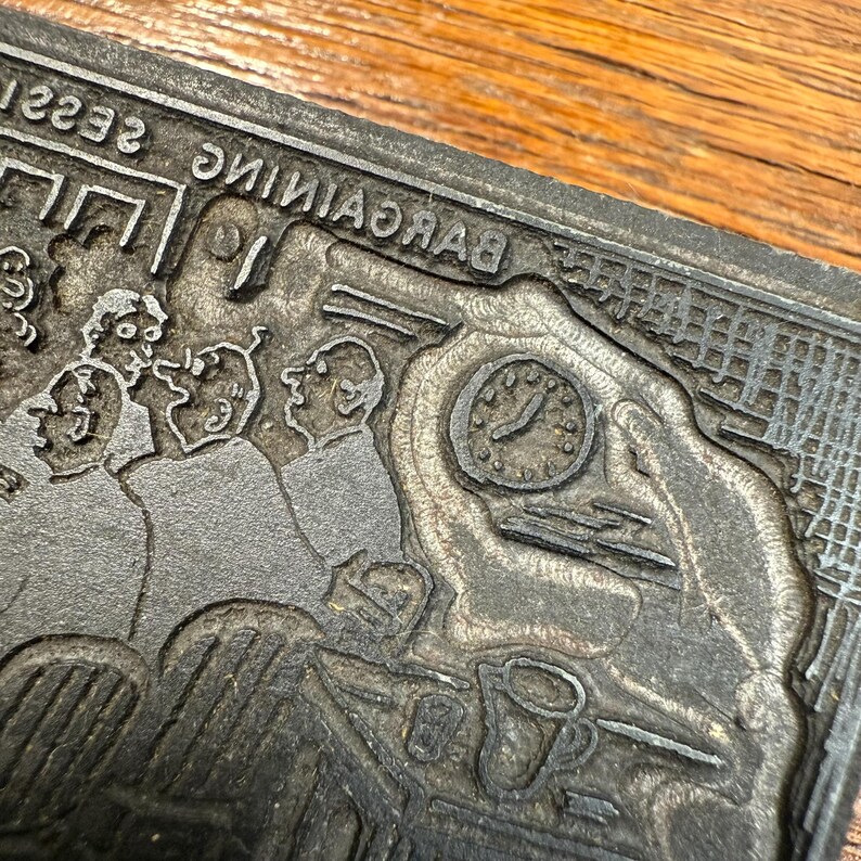 Puede incluir: Un bloque de impresi&oacute;n de metal vintage con una ilustraci&oacute;n detallada de un grupo de personas, un reloj y la palabra "BARGAINING" al rev&eacute;s. El bloque gris muestra signos de desgaste, lo que sugiere su edad y uso.