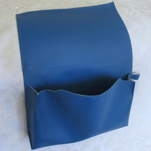 May include: A blue leather pouch with a flap closure. The pouch is folded in half and pinned to a white surface.