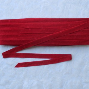 May include: Red velvet ribbon trim, folded and displayed on a white surface. The ribbon is approximately 1 inch wide.