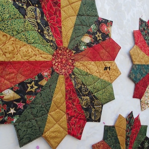 May include: A quilted Christmas table runner with a starburst design in red, gold, and green fabrics. The runner has a center circle with a gold and red pattern. The text '#1' is visible in the upper right corner of the image.