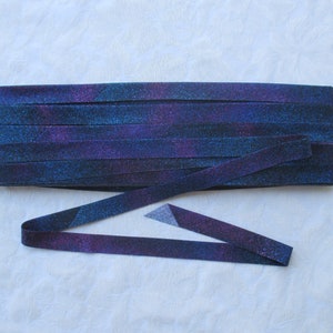May include: A stack of purple and blue fabric strips with a glittery finish. The strips are folded in half and arranged in a row.